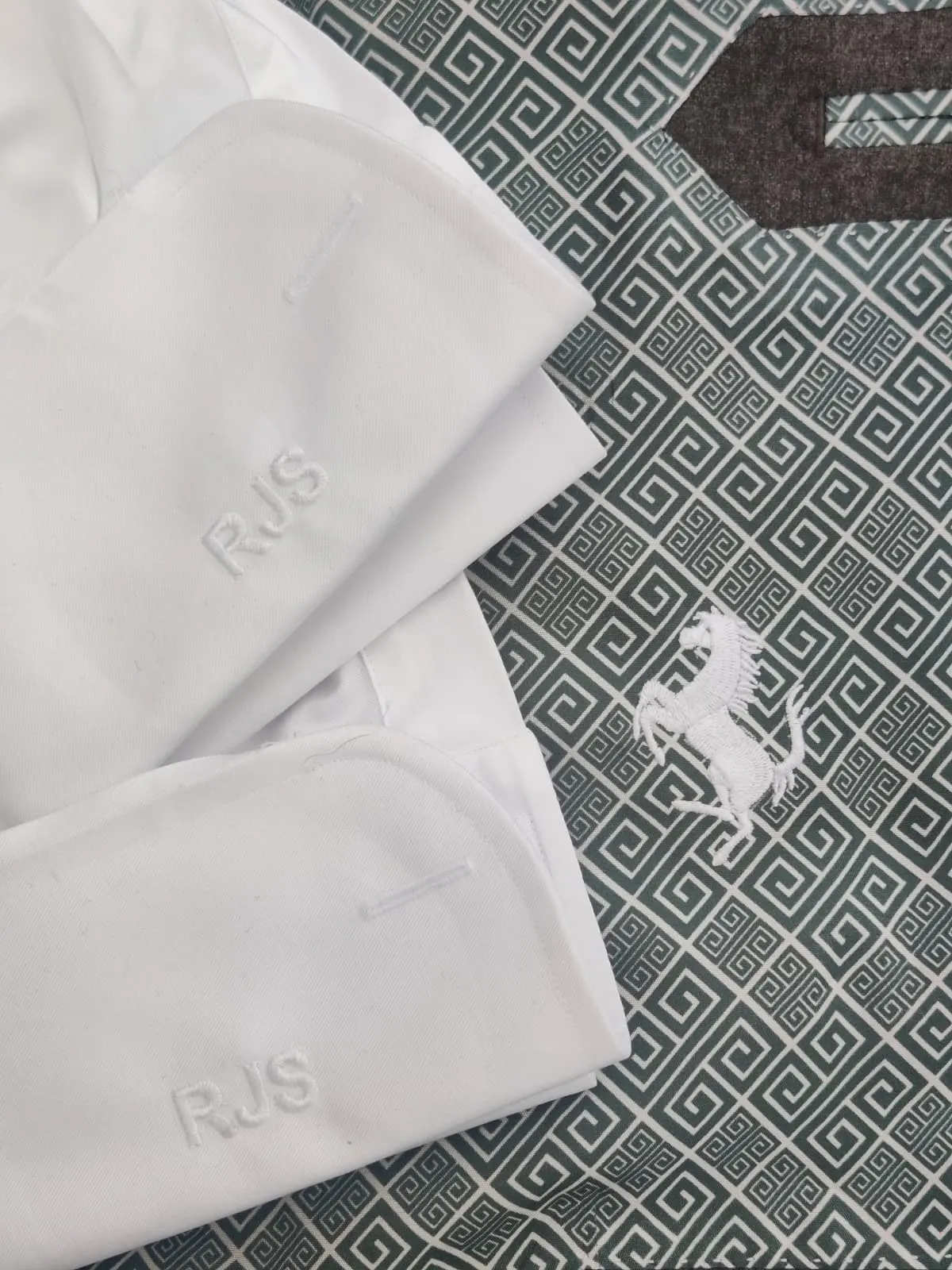 Shirt cuffs monogrammed 'RJS' beside a Ferrari prancing horse logo on patterned fabric